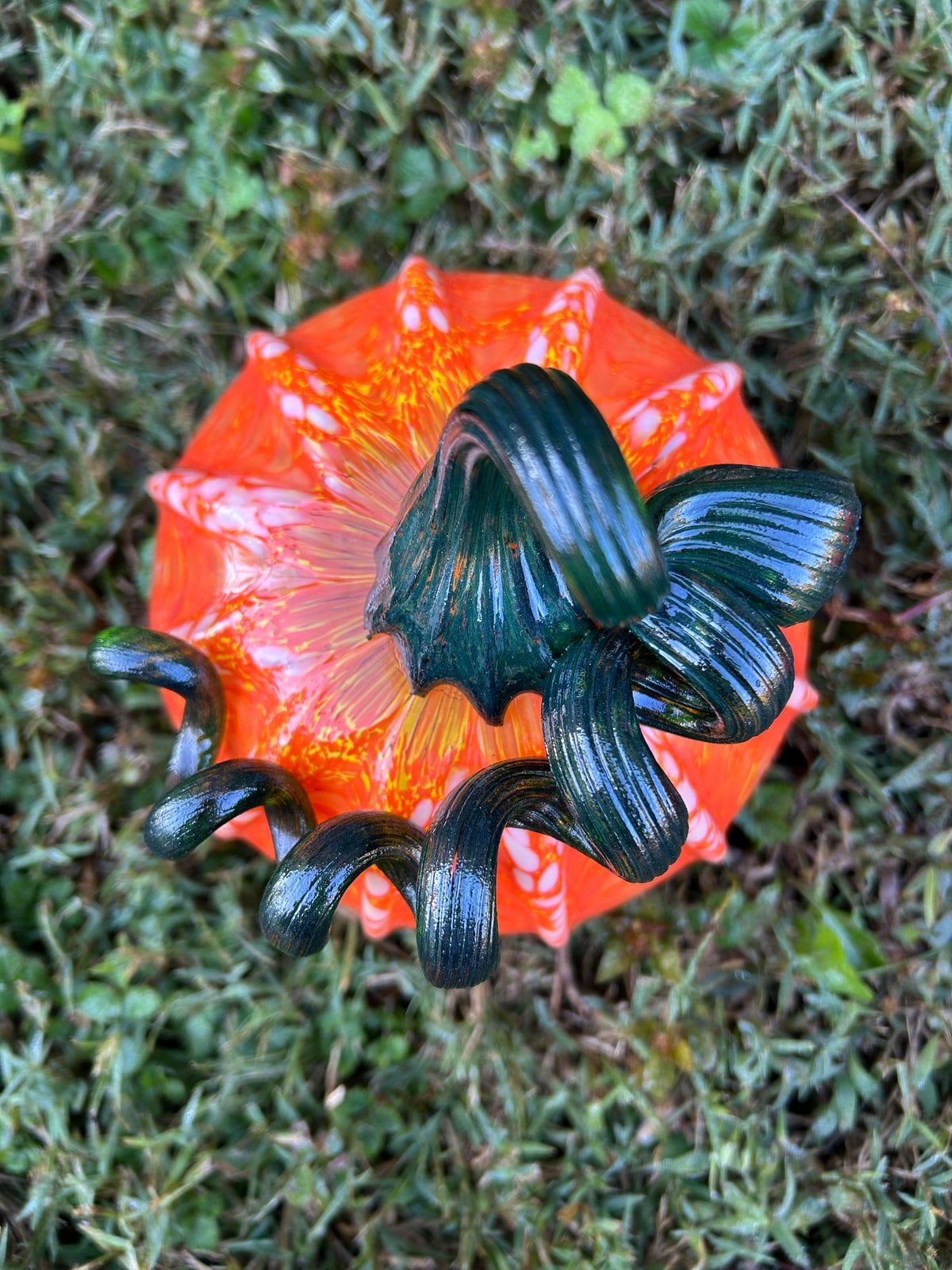 An orange glass pumpkin viewed from above with a dark green curled stem