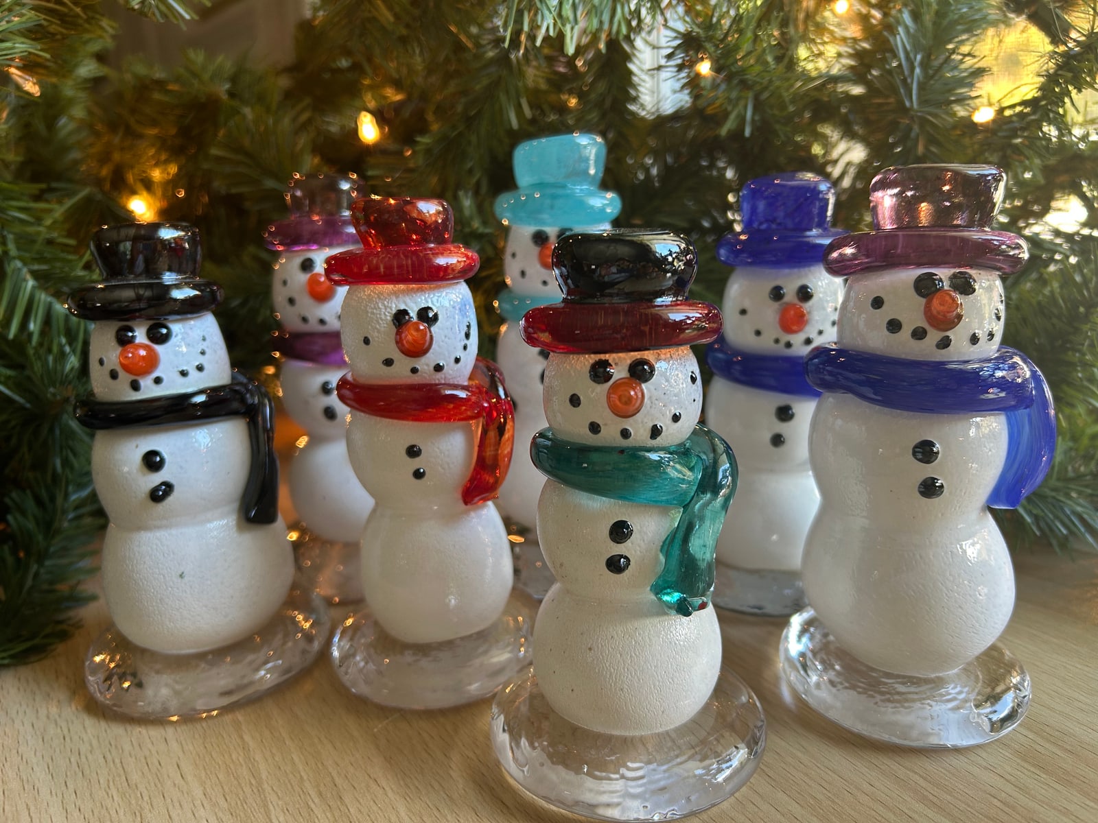 A group of glass snowmen with colourful hats and scarves beneath a Christmas tree